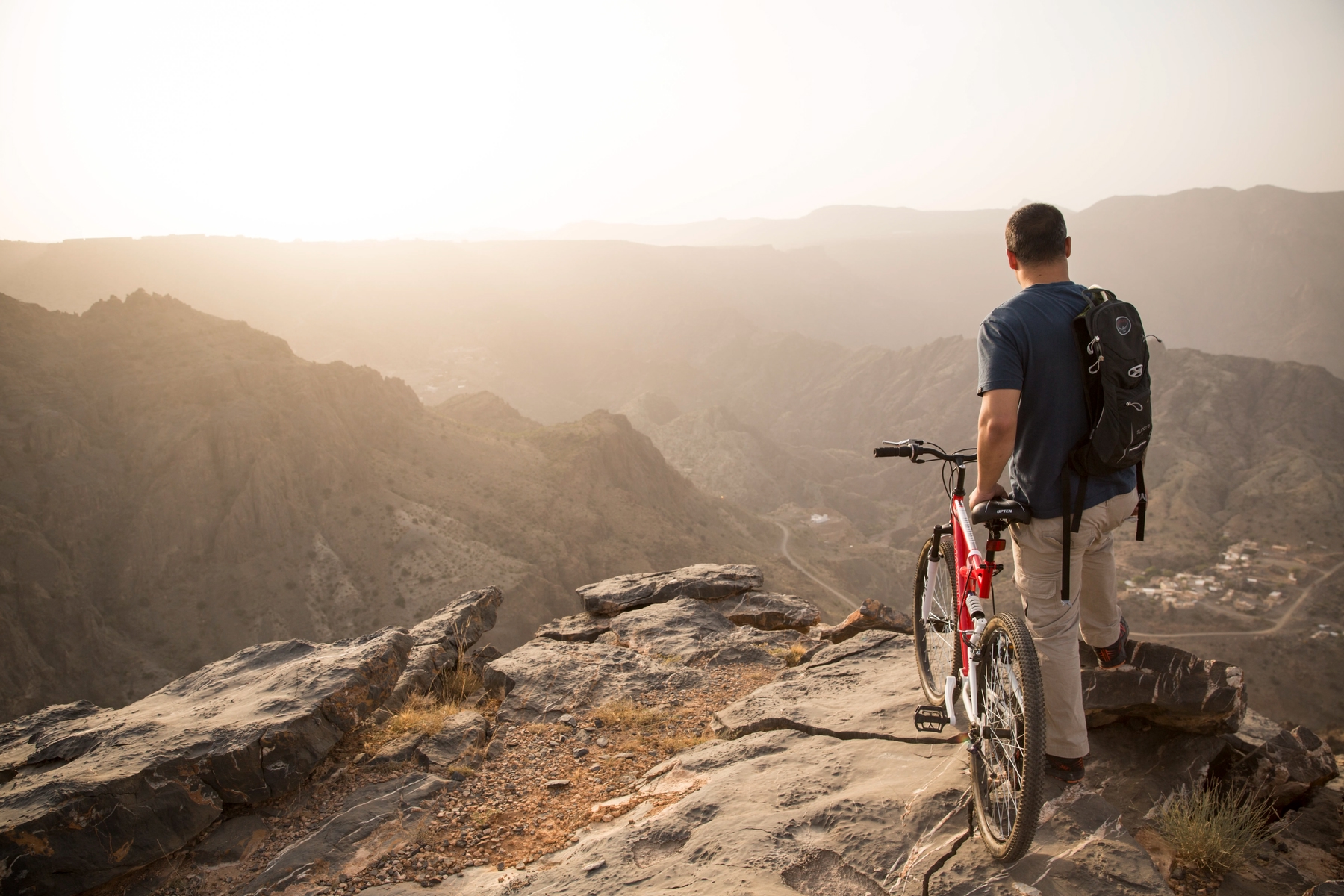 Ein Mann mit Fahrrad blickt auf die Berge des Oman.