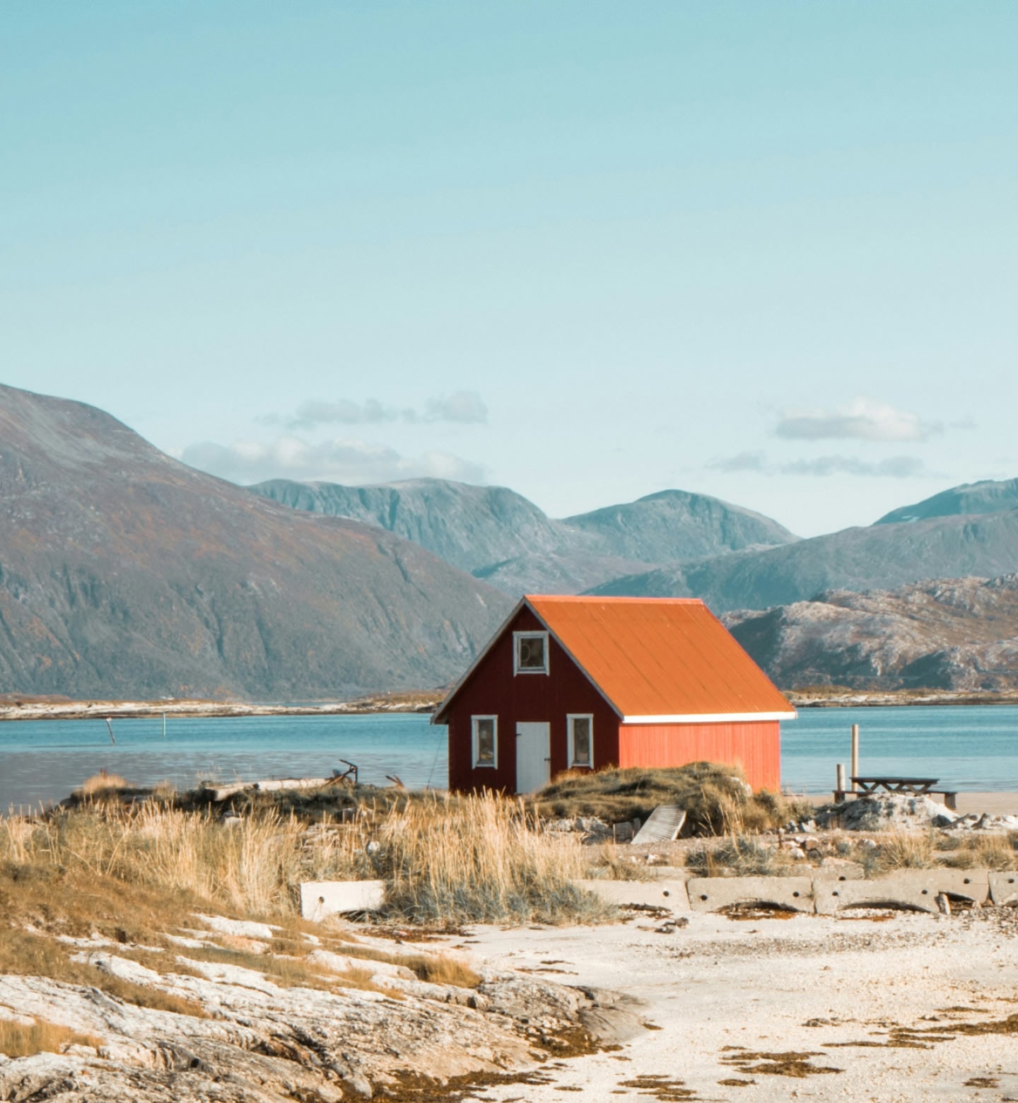 Eine rote Hütte steht an einem ruhigen Fjord nahe Tromsø, Norwegen, mit Bergen im Hintergrund.