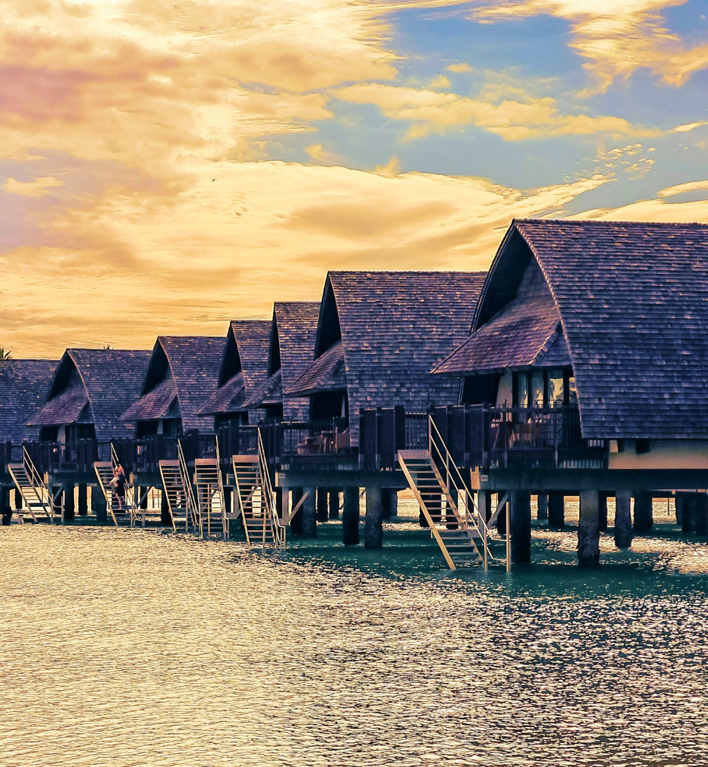 Thatched bungalows on stilts line a glowing tropical lagoon near Nadi, Fiji.