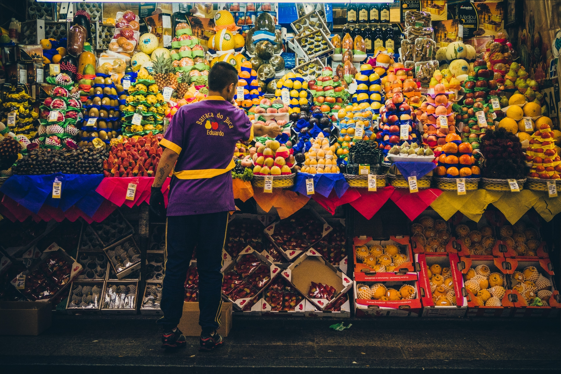 Vendedor em frente aa uma banca de frutas no Mercado Municipal de São Paulo.
