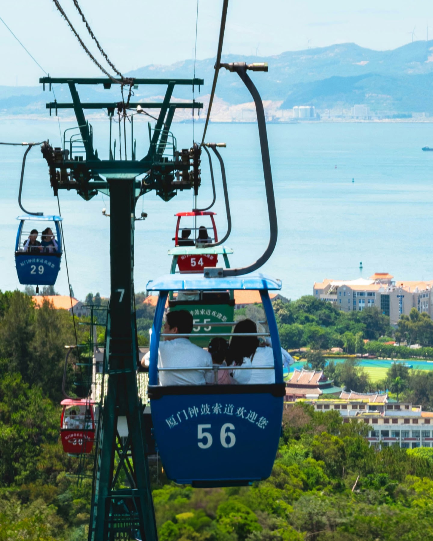 中国・アモイ（厦門）、緑の丘陵と青い海岸線の上を滑るように動くカラフルなケーブルカー。