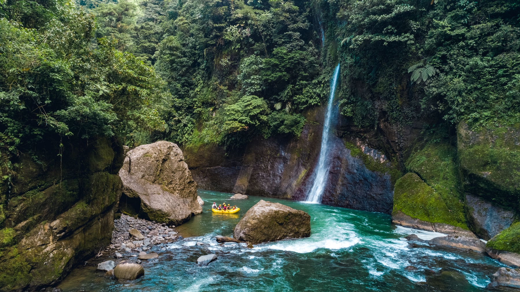 waterfall in Costa Rican jungle with tourists rafting in the background.