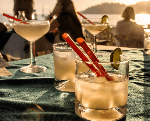 A close-up view capturing the laid-back charm of a beach bar table adorned with four expertly crafted cocktails, each drink exuding tropical allure and inviting relaxation against the scenic backdrop of the seaside ambiance.