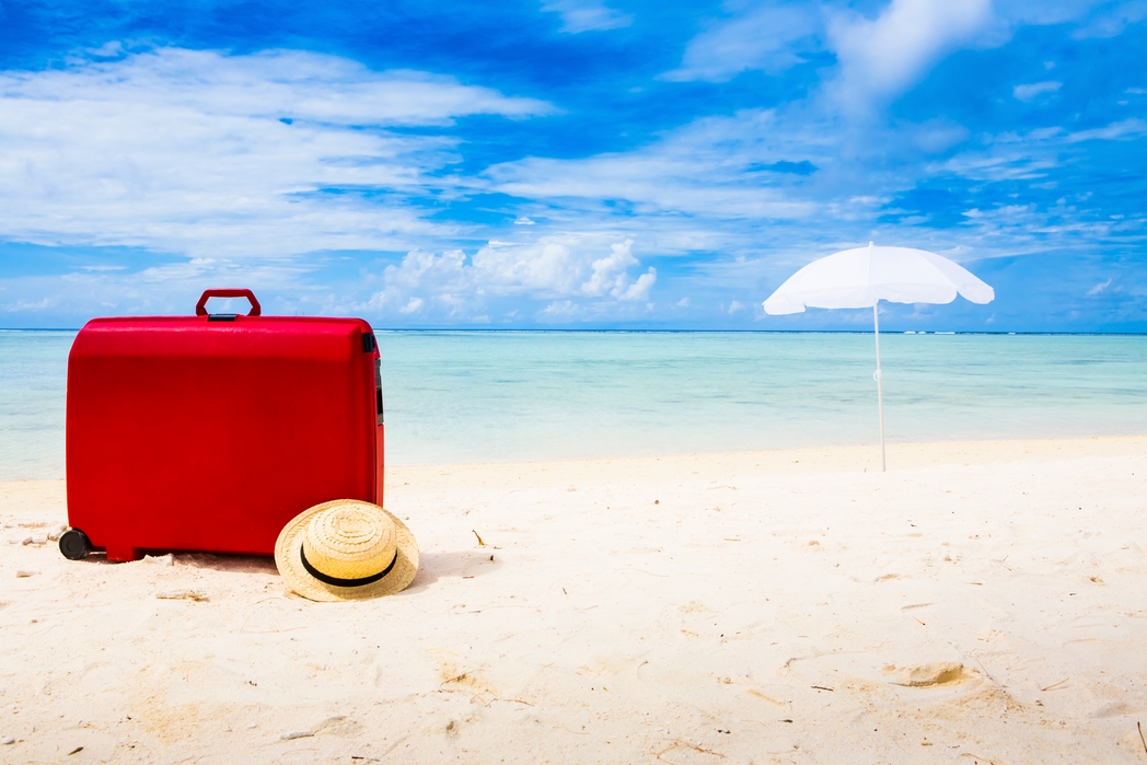 Red suitcase and a hat on a beach - buying a lightweight suitcase is one of the top travel tips for your holidays