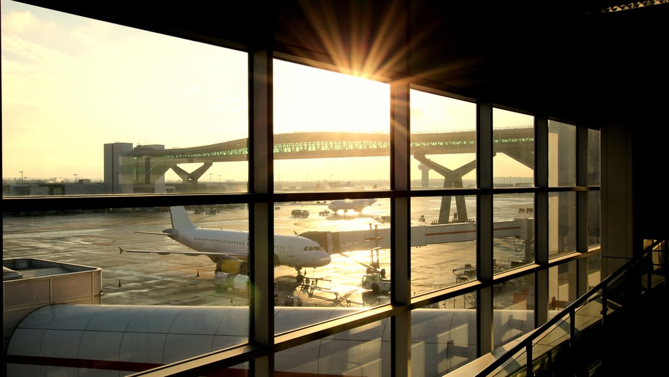 Ein Flugzeug auf dem Rollfeld bei Sonnenaufgang, sichtbar durch große Fenster.