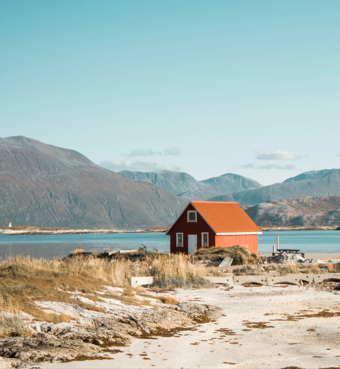 A red cabin stands by calm fjord near Tromso, Norway with mountains in the background.