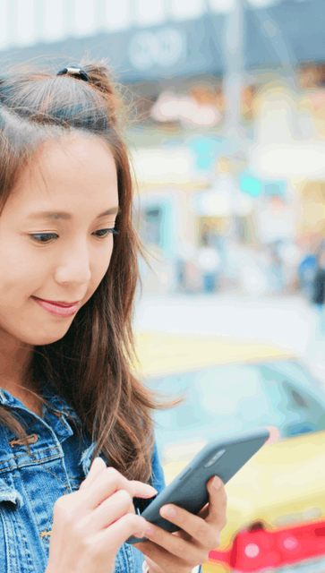 A woman checking her Tokyo travel guide on her phone while she waits at the side of the road for a taxi. 