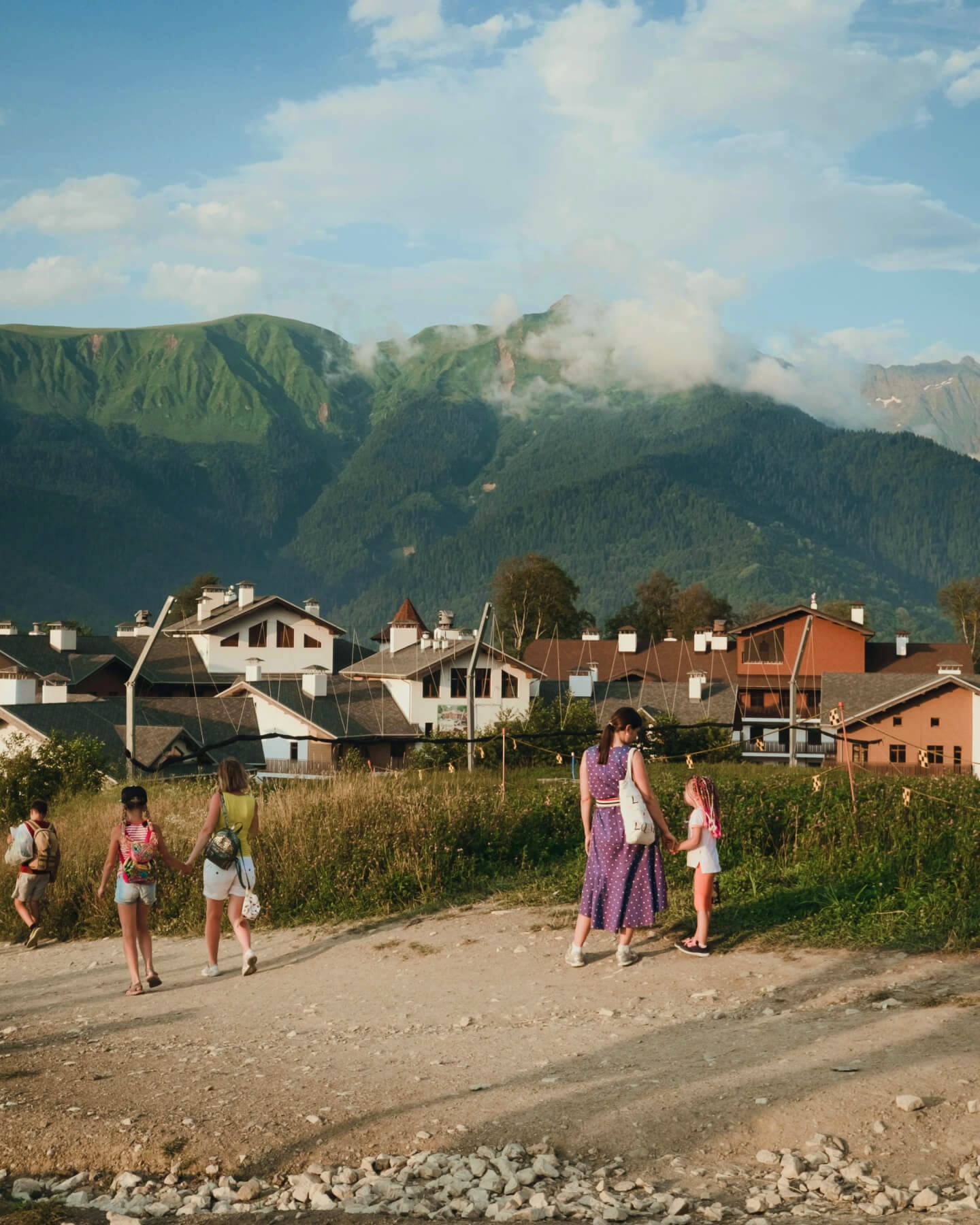 Several women and children walking along a stone path next to a mountain village