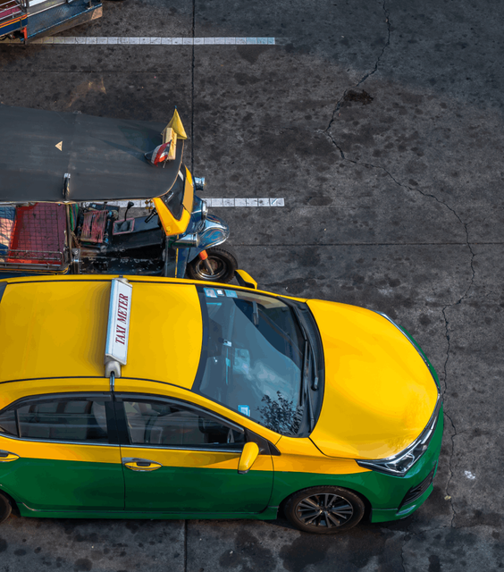 An aerial view captures a vibrant scene featuring a yellow and green Thai taxi positioned alongside a colorful Tuk-Tuk.