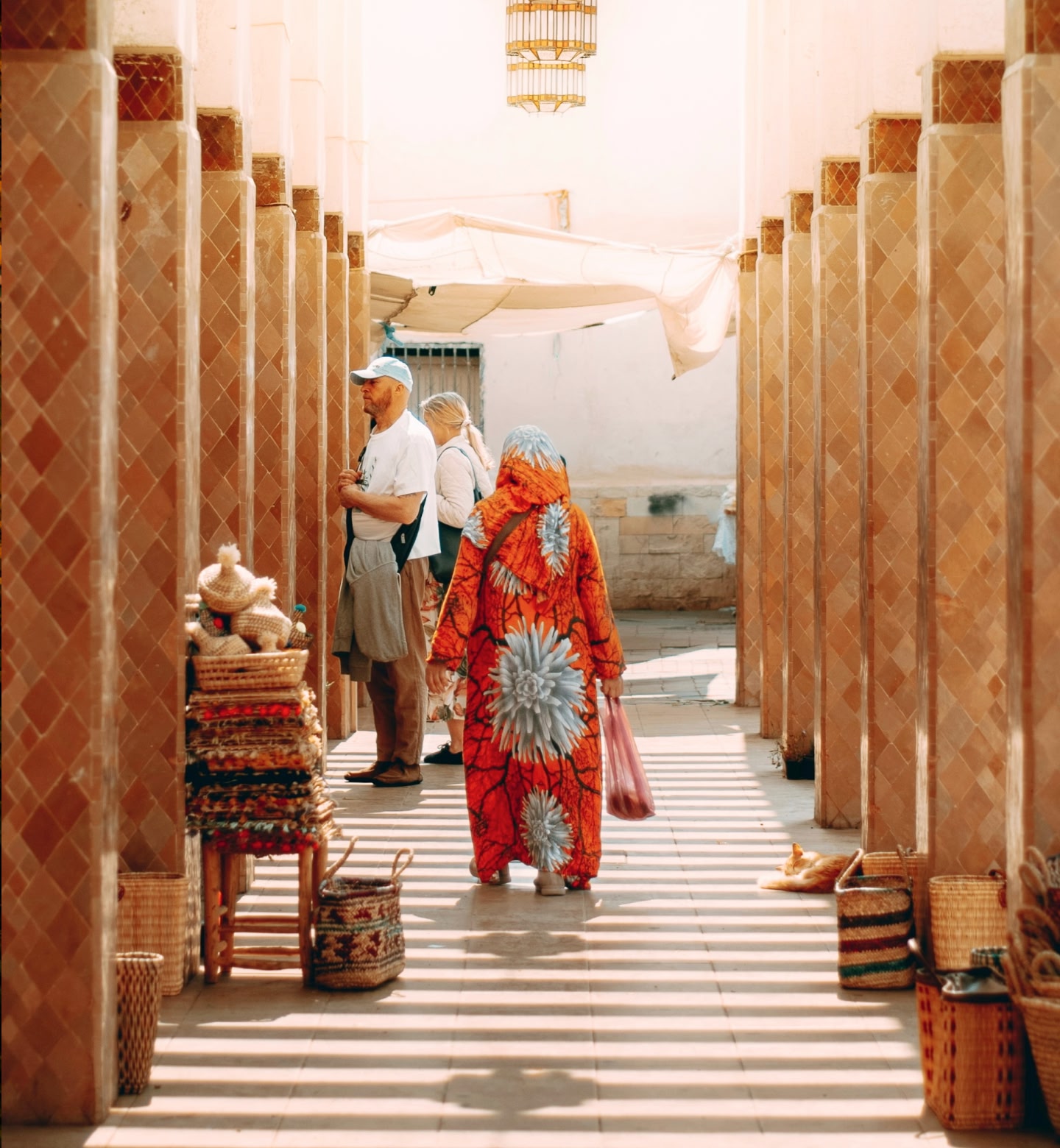 People shop in a sunlit market lined with handmade goods in Agadir, Morocco.