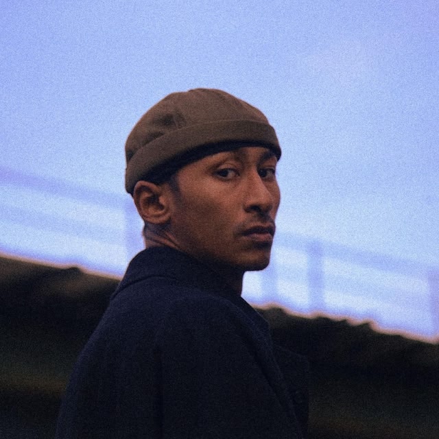Singer Jitwam wearing a hat looking out to the distance 