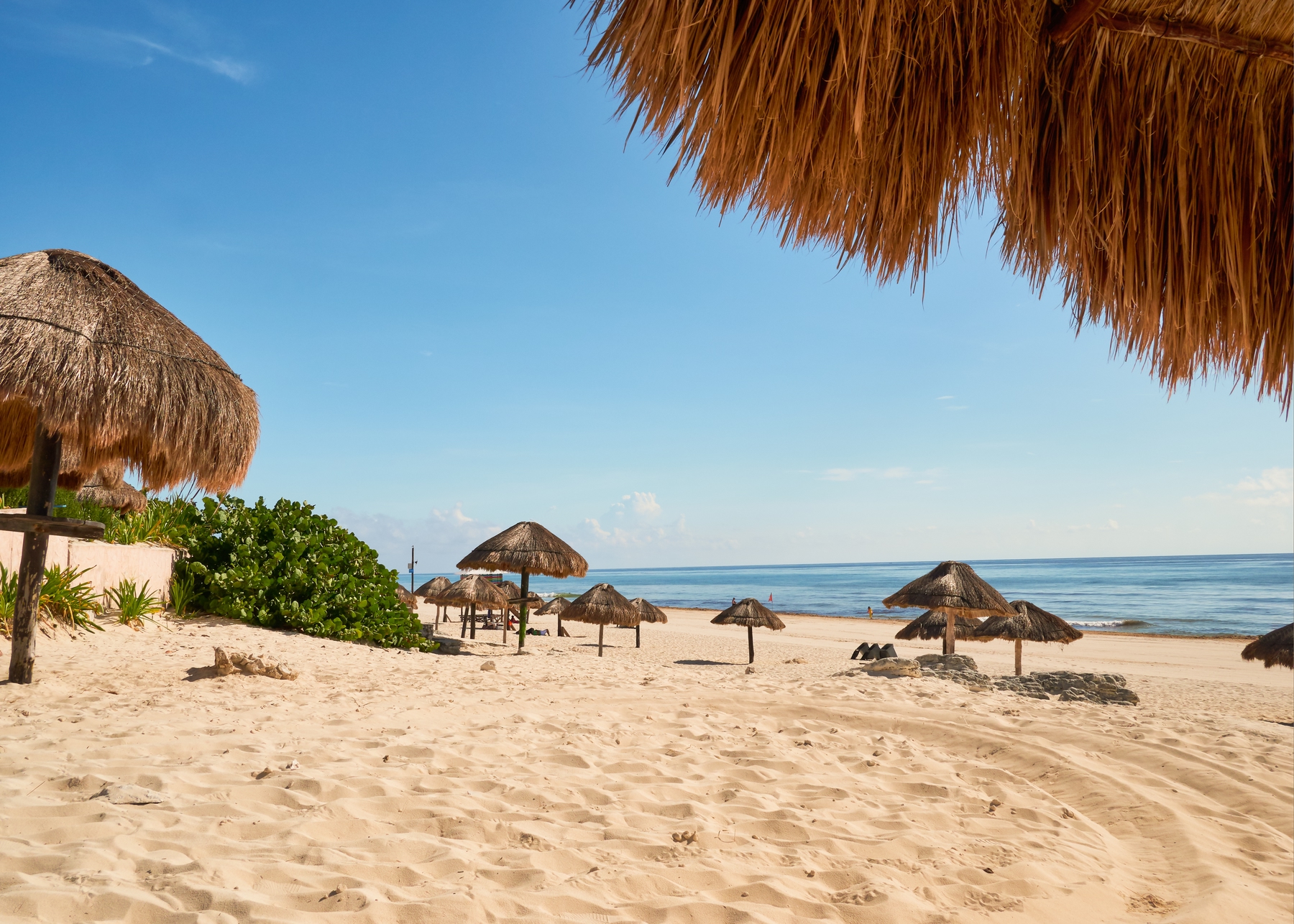 View of the water from a golden-sand beach with shaded huts dotting the beach.