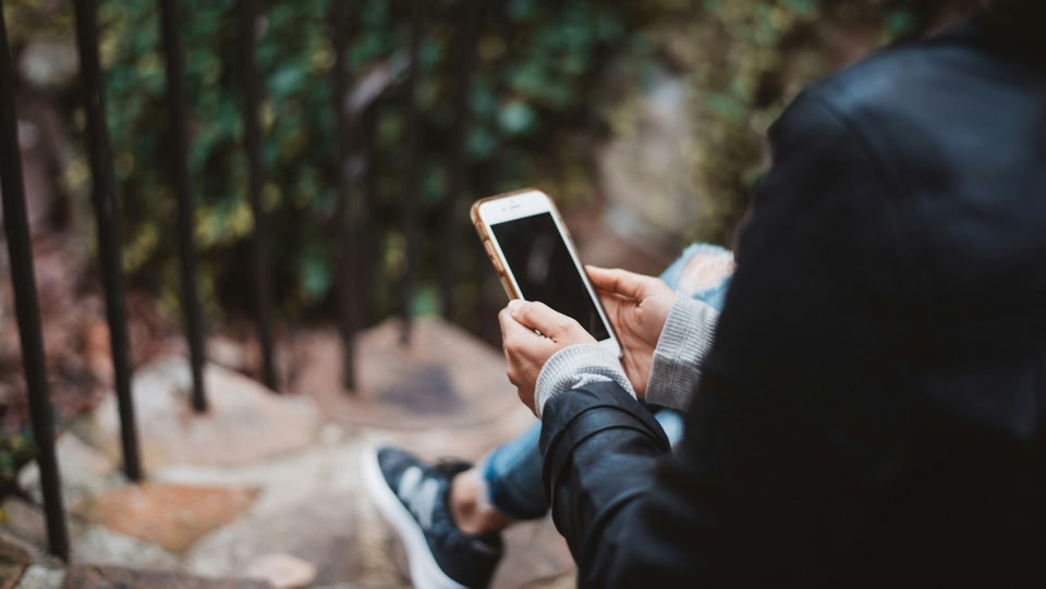 Person sitting on a step outside and holding a smartphone