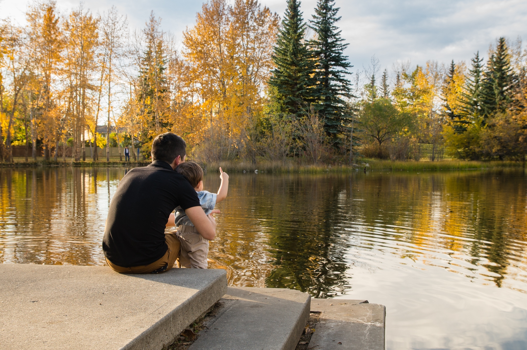 man and boy by a lake pointing at the fall leaves