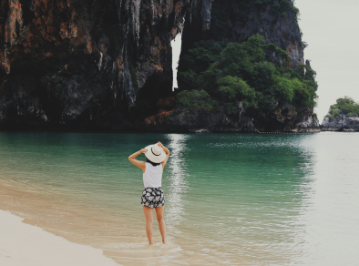 Eine fesselnde Fernaufnahme einer Frau, die die ruhige Schönheit des Meeres genießt, während sie im kristallklaren Wasser paddelt und dabei einen stilvollen weißen Sonnenhut trägt.