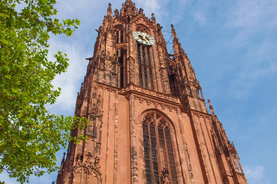 Frankfurt cathedral shot from below, with blue sky behind and a green tree to the left.
