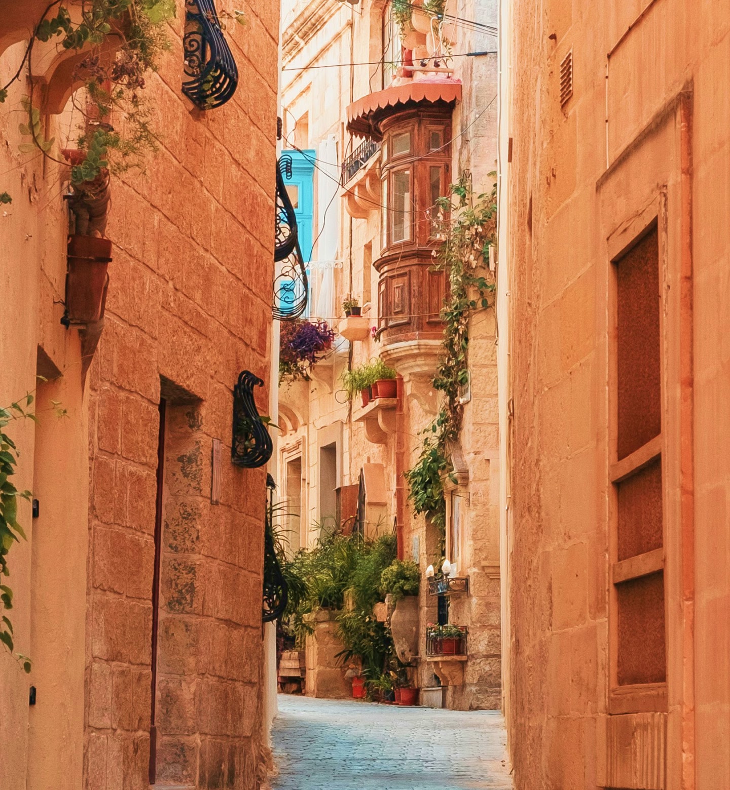 Eine Gasse mit Steinmauern, gesäumt von Balkonen und Blumentöpfen in Valletta, Malta.