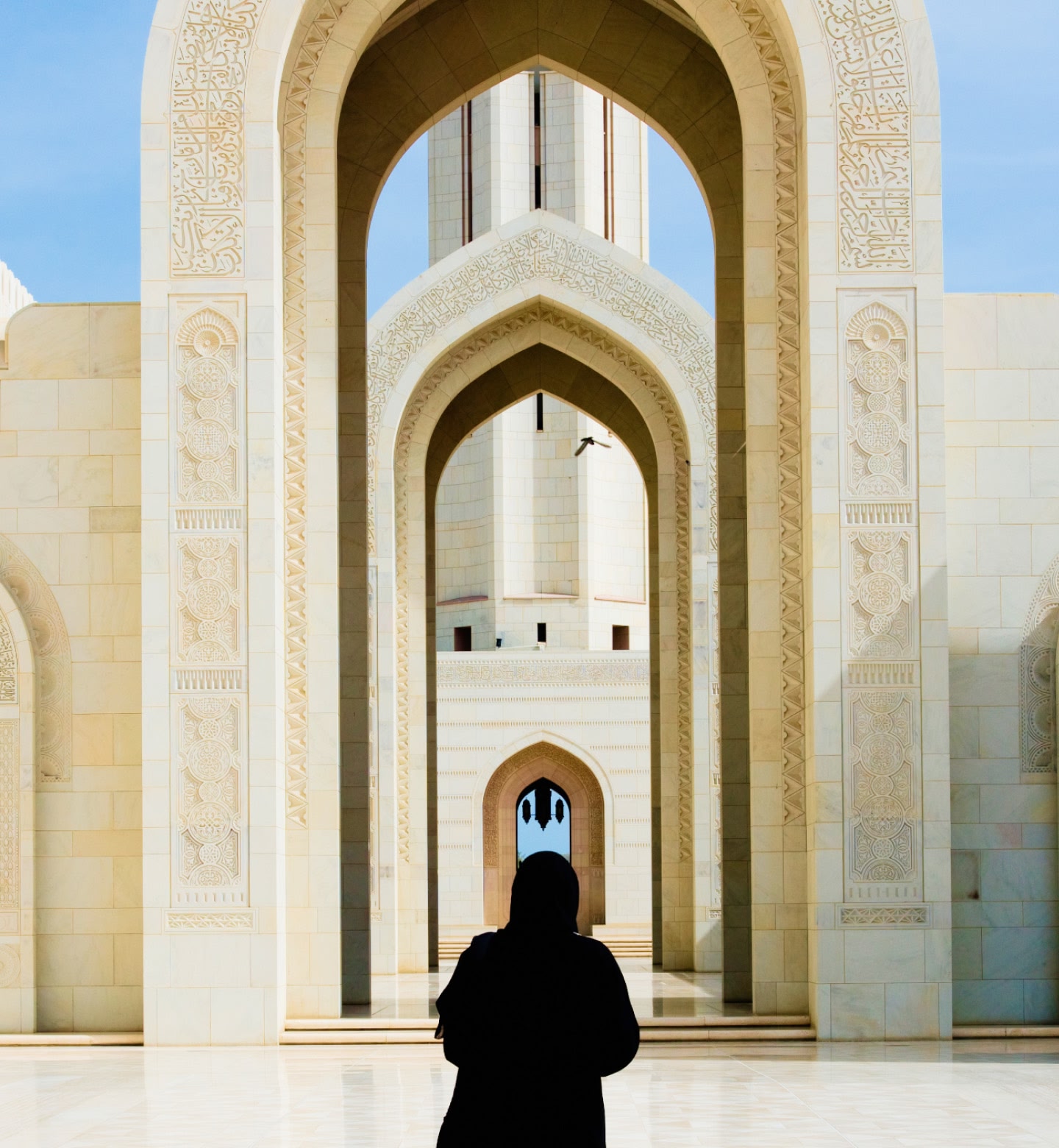 La sagoma di una donna sotto gli archi bianchi decorati di una grande moschea a Mascate, in Oman.