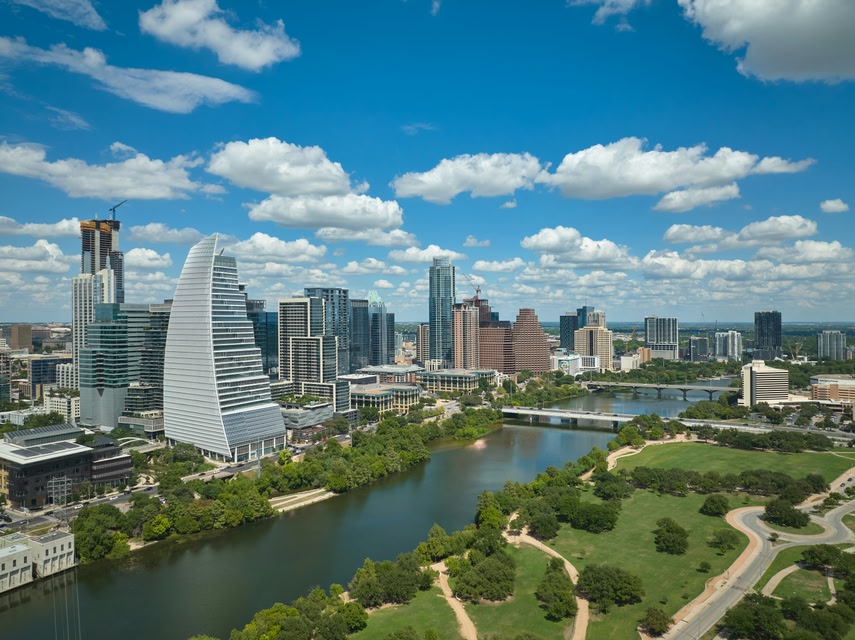 Aerial view of the Austin, Texas, skyline on a sunny day, showing skyscrapers, water, and green spaces.