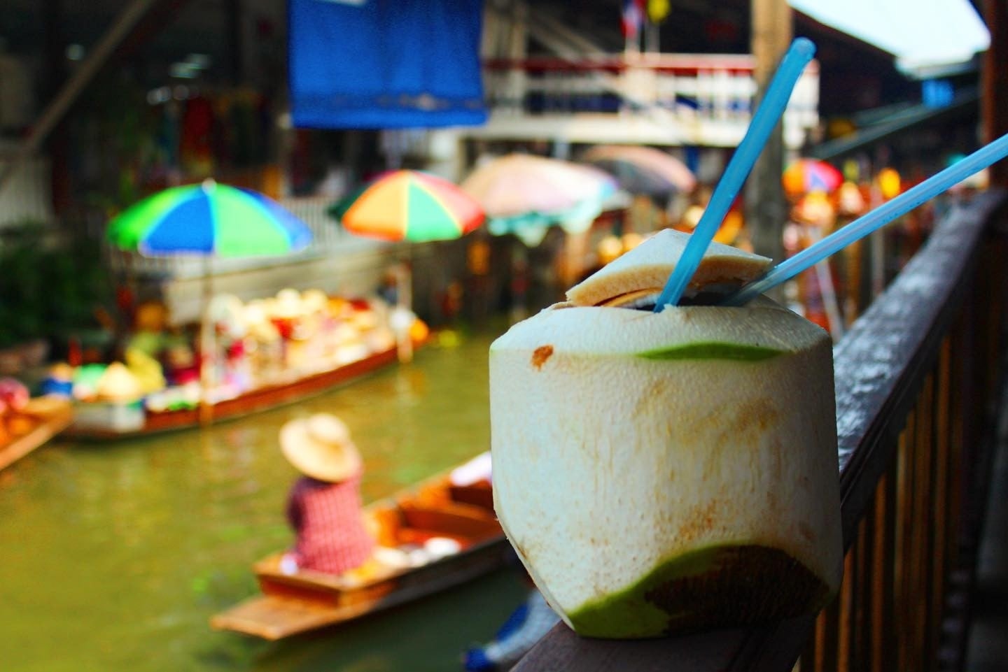 close up image of a coconut and a Thai river market blurry in the background.