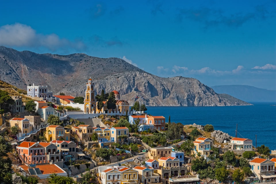 Εκκλησία στη Σύμη. Παραδοσιακά σπίτια και θάλασσα στο βάθος