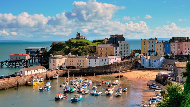 and image of a beach with boats in the sea and colourful buildings surrounding the beach