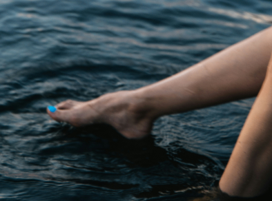 Eine ruhige Aufnahme der Füße einer Frau im tiefblauen Meer, sanfte Wellen umspülen ihre Zehen.
