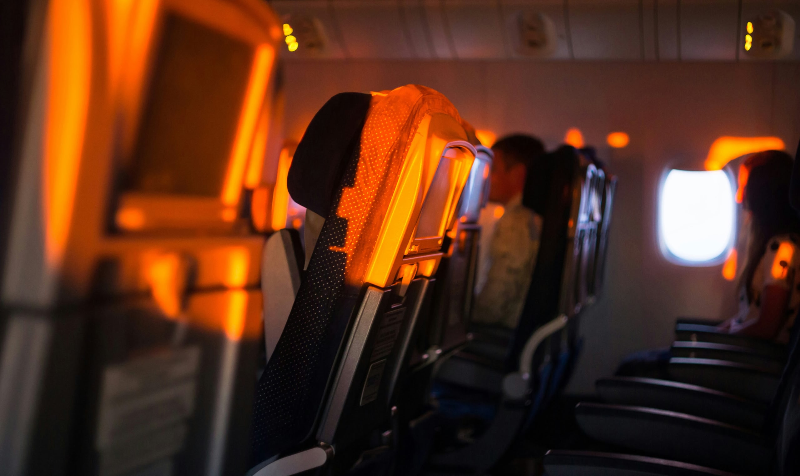 オレンジ色の陽光が窓から差し込む飛行機の空席の列。