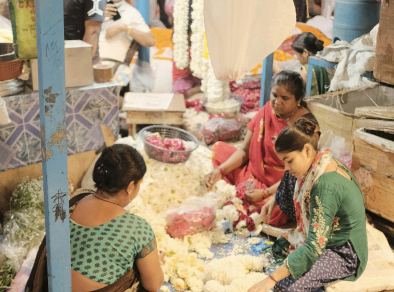 A captivating image of skilled workers handcrafting intricate flower ornaments amidst the vibrant hustle and bustle of a Mumbai street market.