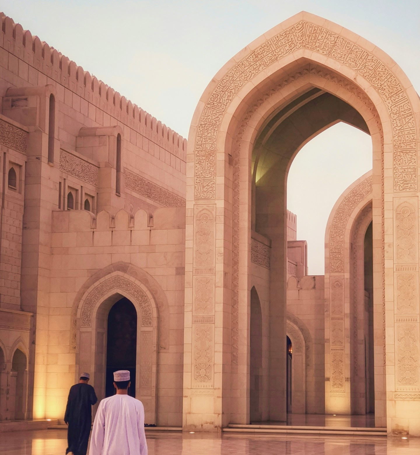 Two men walk through towering arches of Muscat’s Grand Mosque, Oman.