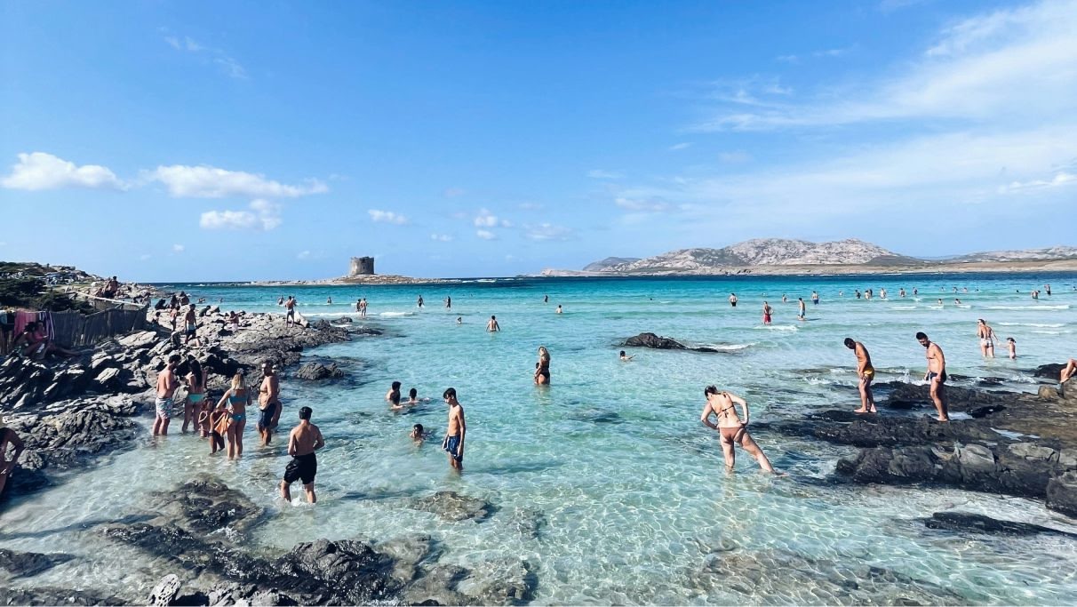 Uma praia movimentada com um afloramento rochoso e muitos banhistas felizes