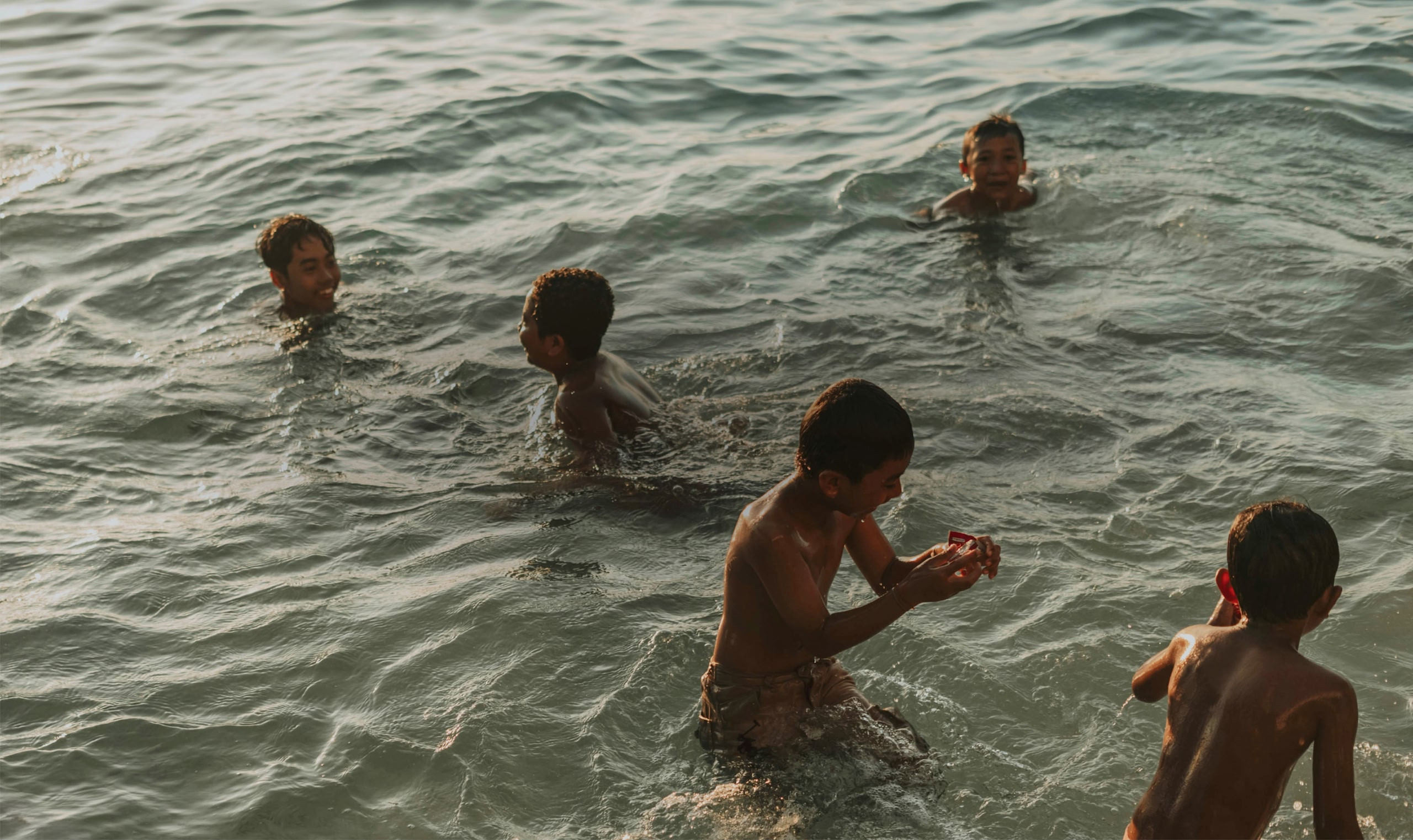 Cinco meninos brincando no mar.
