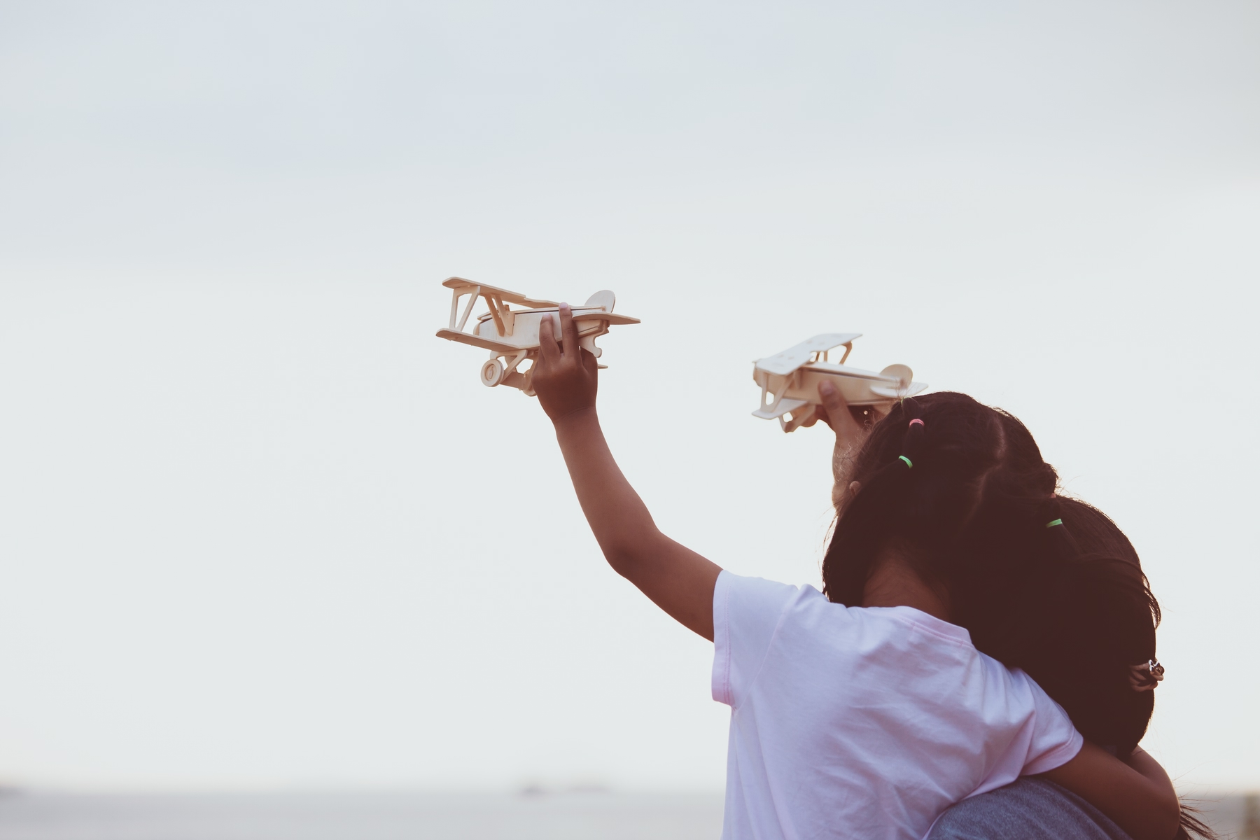 Child girl and her mother hugging and playing with toy wooden airplane