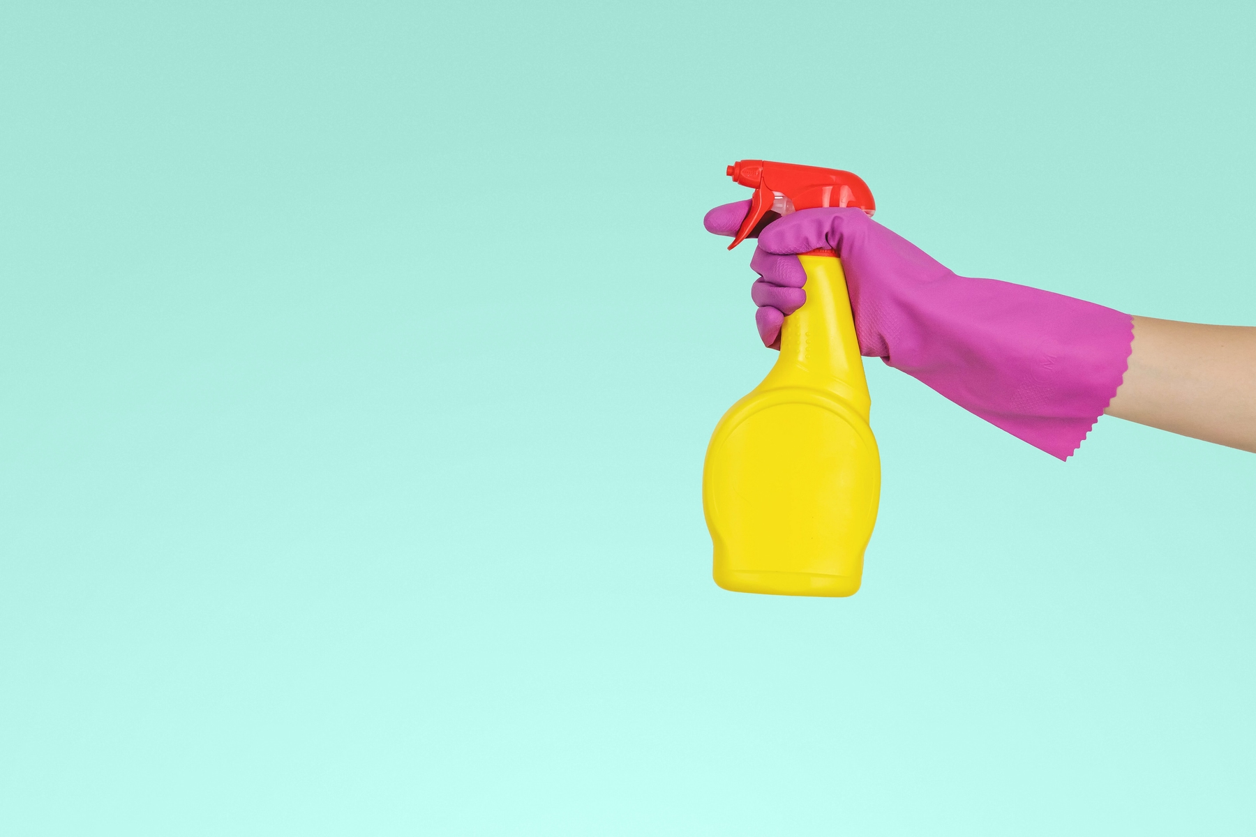 A gloved hand is holding a yellow cleaning spray bottle.