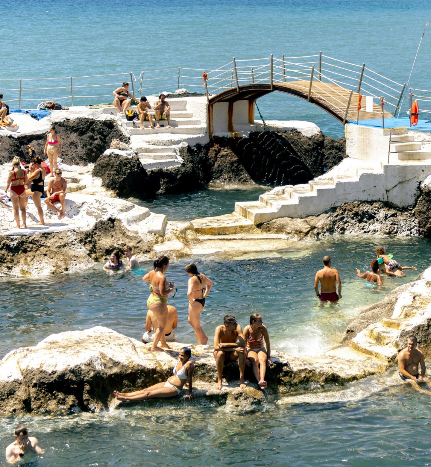 People swim and sunbathe in rocky pools by the ocean in Madeira, Portugal.