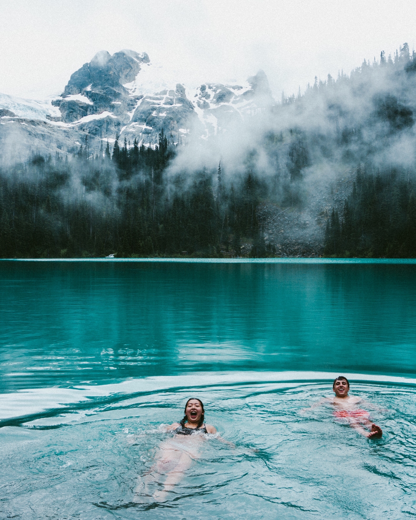 Couple swimming in hot springs with a snow-capped mountain in the background
