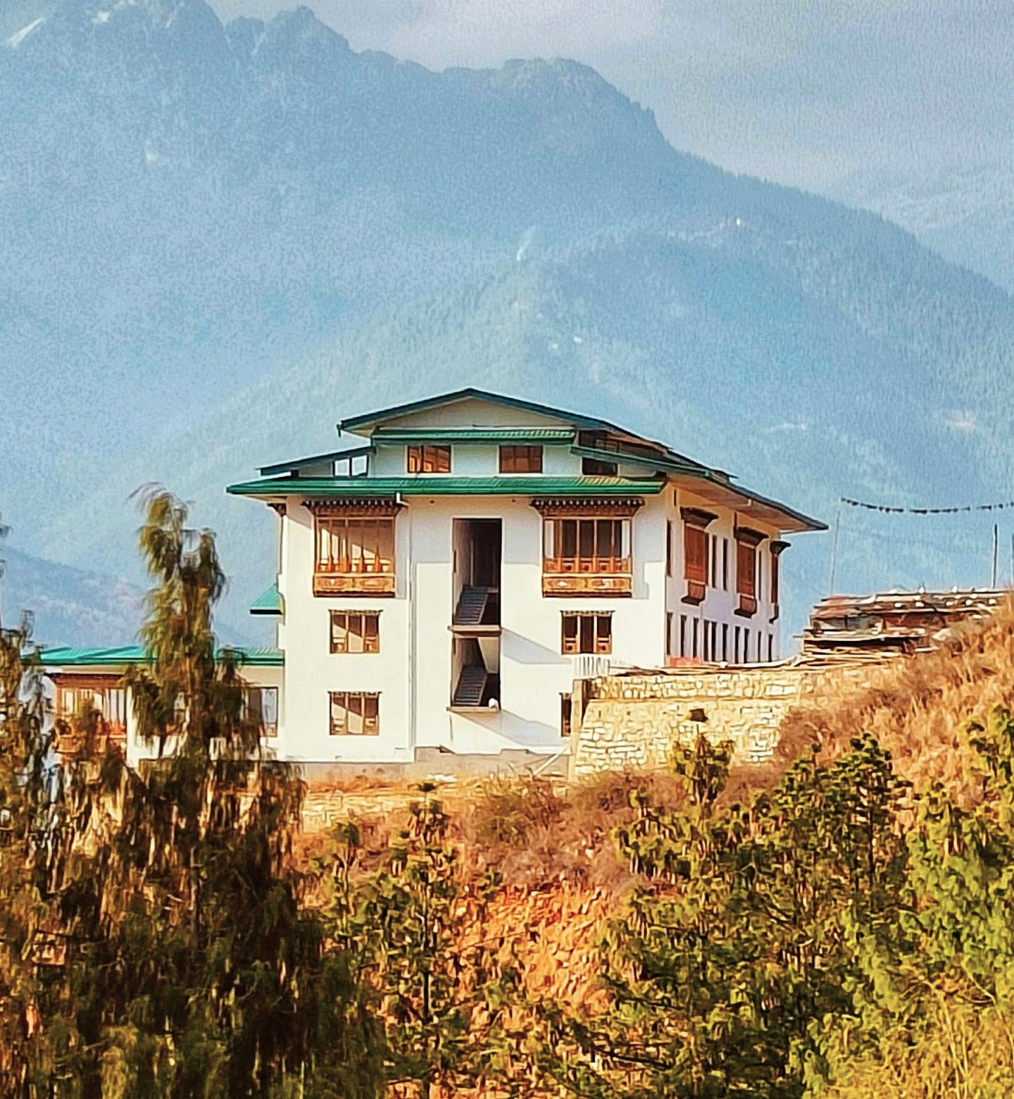 ブータン、パロの霧深い山々を背景にした丘の上の建つ、緑の屋根の白い家。