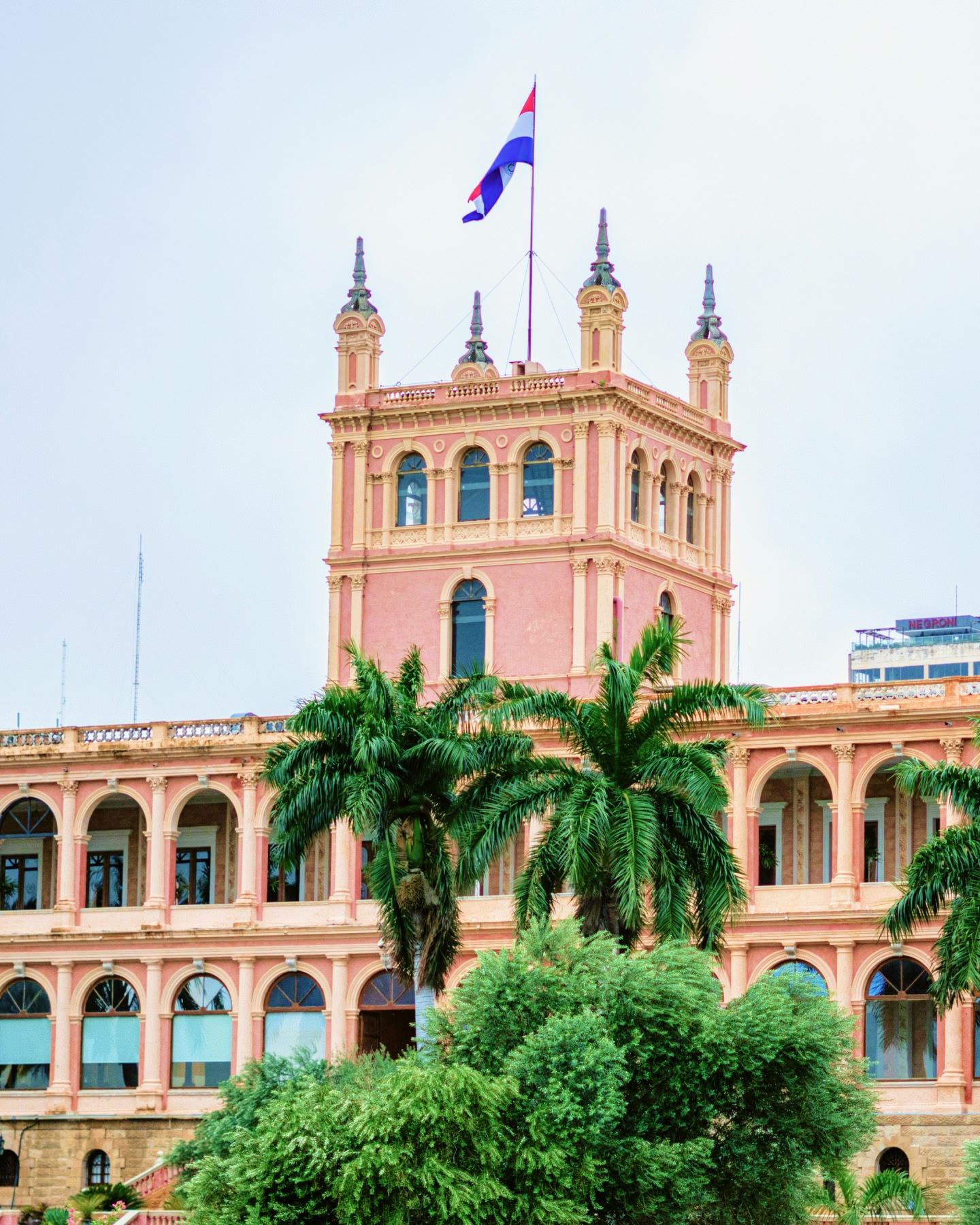Um edifício rosa com palmeiras e uma bandeira no topo em Assunção, Paraguai.