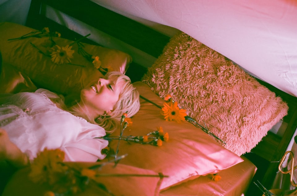 Singer Ny Oh lying on a bed with flowers 