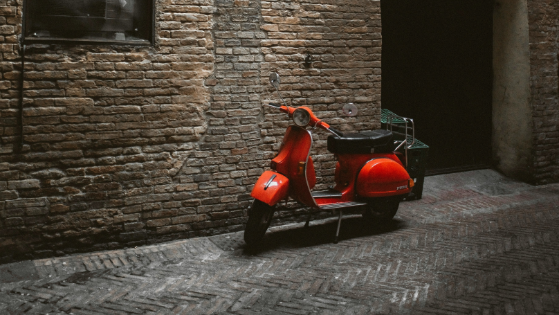 Scooter vermelha italiana estacionada em frente a um prédio em Roma