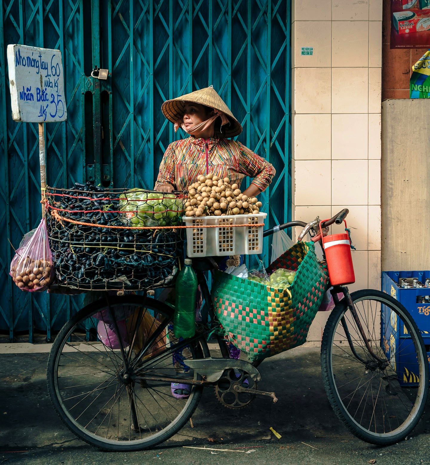 A woman in a traditional Vietnamese sunhat stands next to a bicycle loaded up with fresh produce in Ho Chi Minh City, Vietnam.