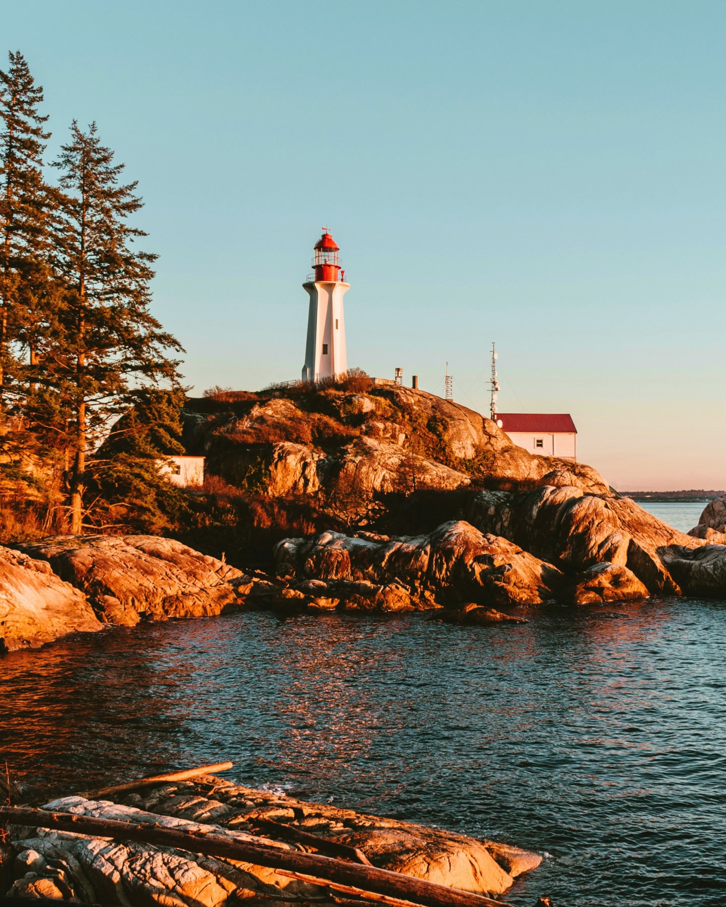 Red and white lighthouse perched on coastal rocks at sunset in Vancouver.