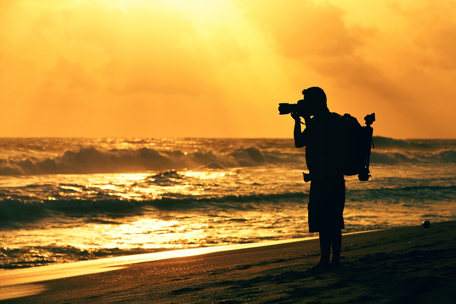 man holding a professional camera at sunset by the beach