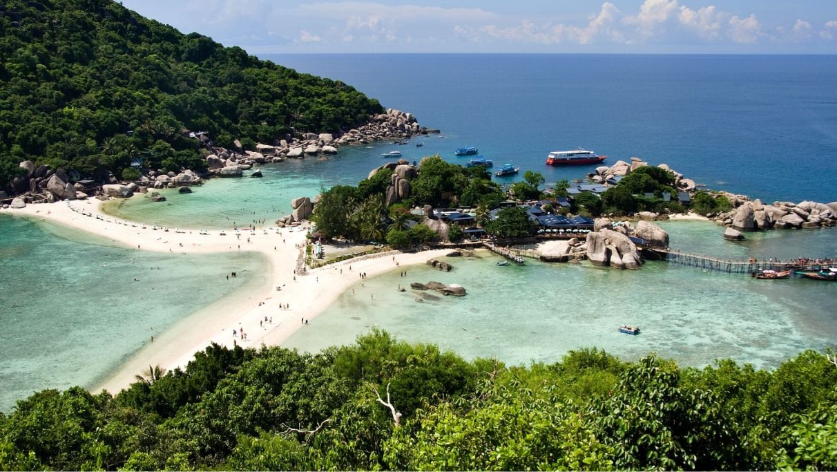 Thail beach surrounded by natural and green landscapes with the blue ocean during daytime. 