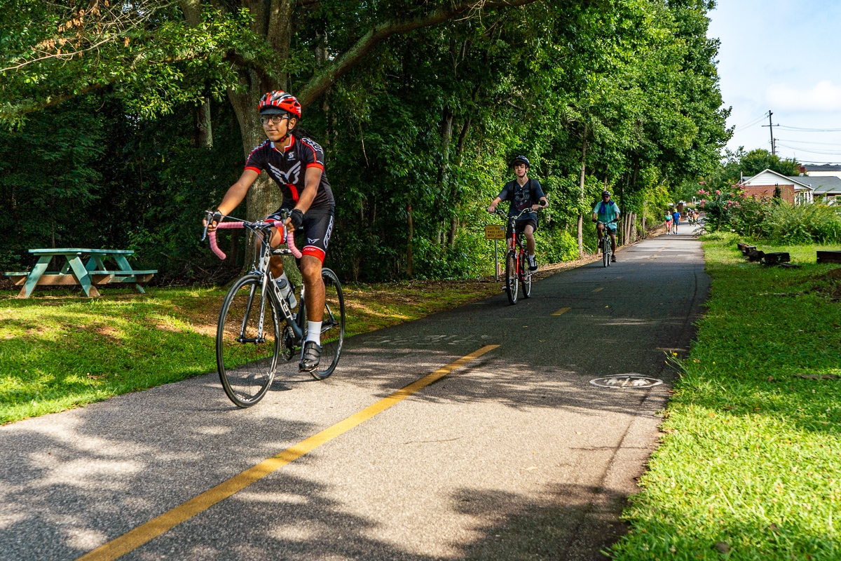 People biking in a row on bike path in the middle of green space