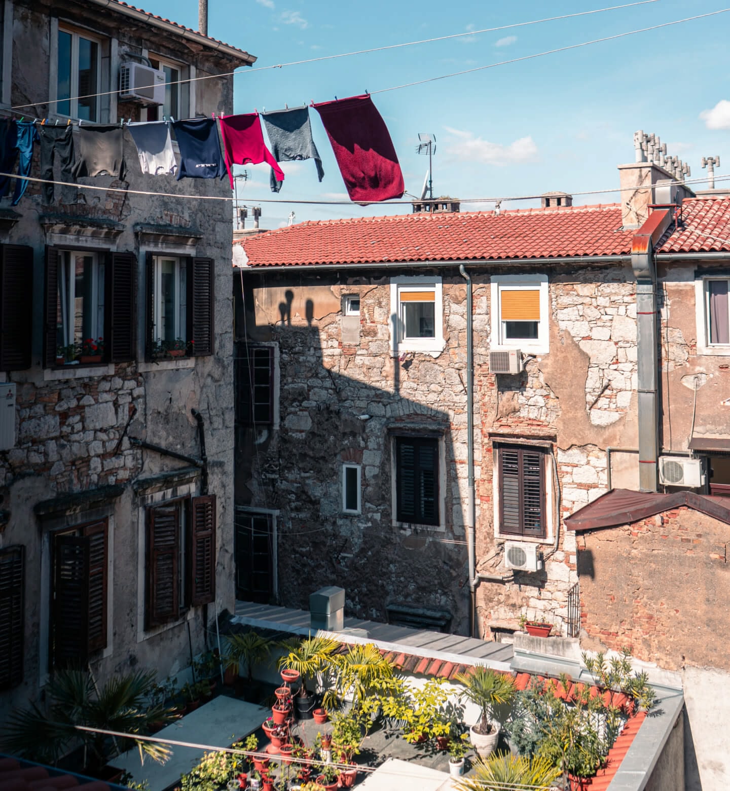 Clothes drying on a line above a brick courtyard filled with potted plants in Rijeka, Croatia