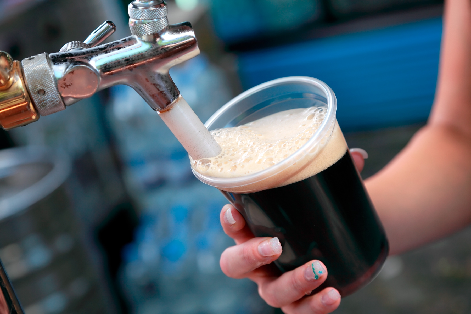 Dark beer being poured from a tap in a plastic cup