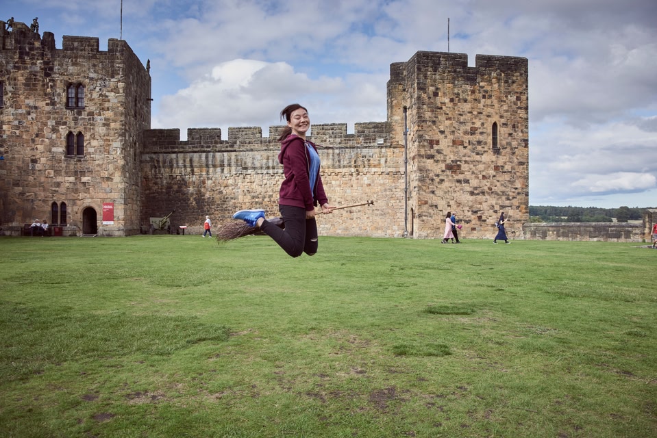 Young woman hovering on a broomstick in the Outer Bailey of Alnwick Castle, Northumberland.