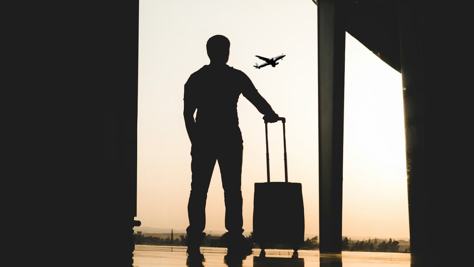A man watching an airplane taking off from an airport window.