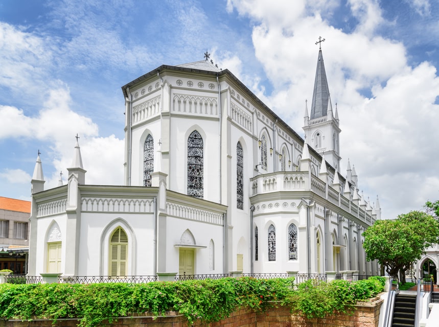 Amazing white colonial building of old catholic church in downtown of Singapore. Gothic-style chapel on blue sky background and other elements of classical architecture.